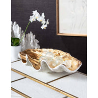 Large golden clam shell decorative bowl with a textured white exterior, holding clear glass orbs.