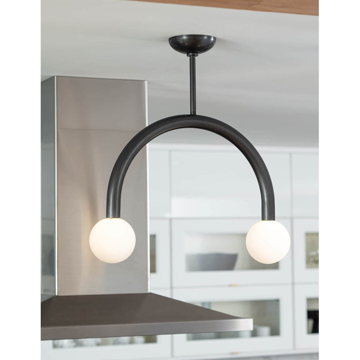 Happy Pendant Small in oil rubbed bronze, featuring a curved metal frame and two matte white glass globes.
