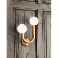 Happy Sconce Left Side in natural brass with two matte white glass globes on a wooden wall.