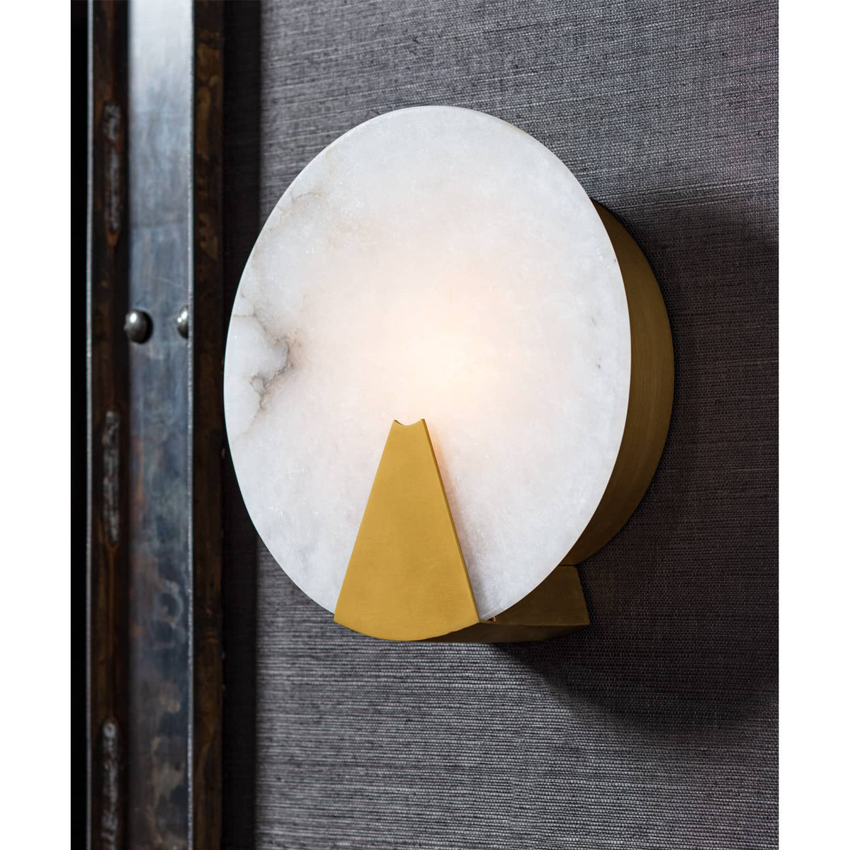 Round Houston sconce with natural alabaster diffuser and brass framing, mounted on a dark textured wall.