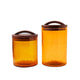 Two amber glass canisters with wooden lids on a white background