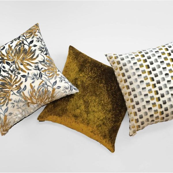 Three luxury designer throw pillows: a 24" mustard multi floral, a solid mustard velvet, and a white and gray geometric.