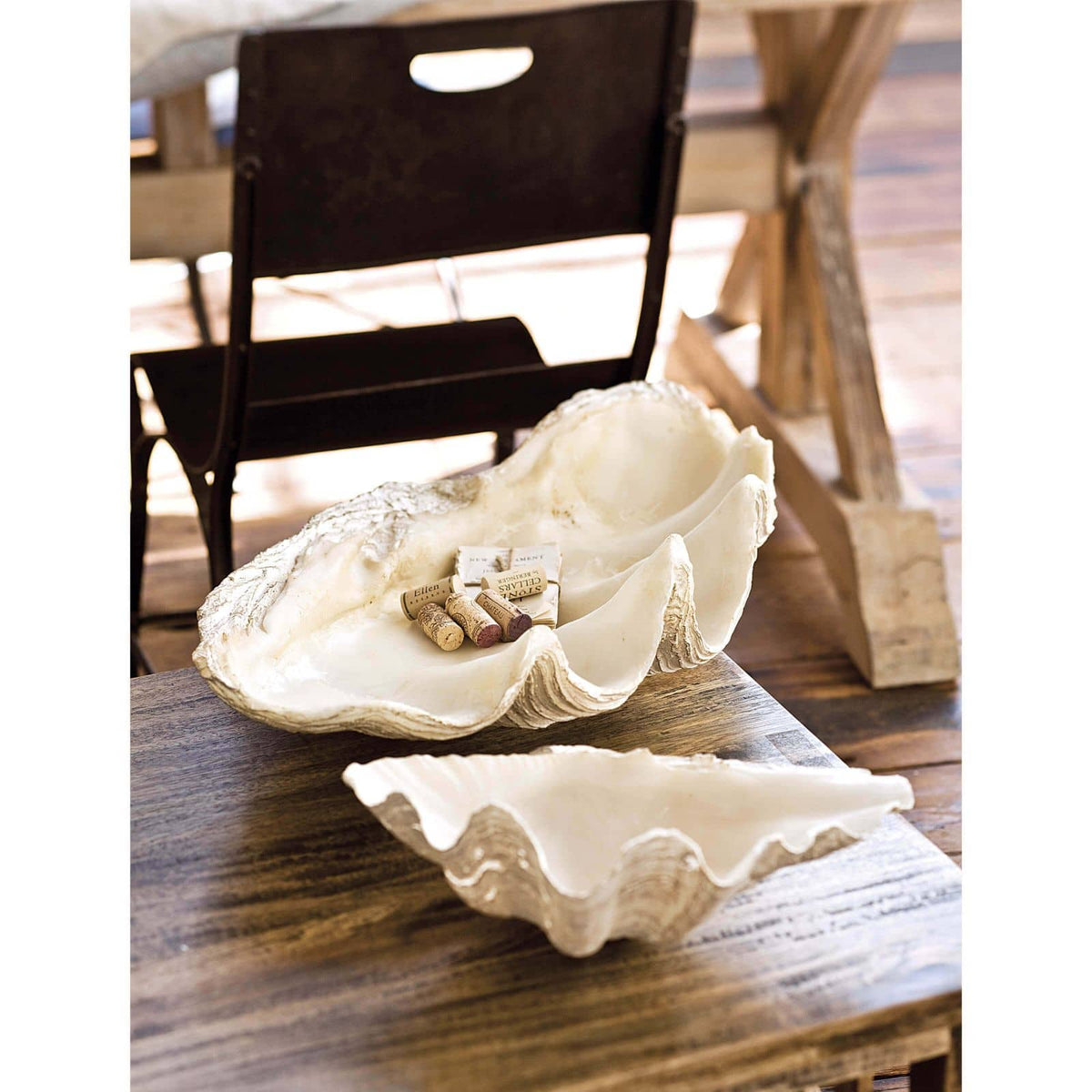 Large white resin clam replica bowl with smaller clam dish on a wooden table.