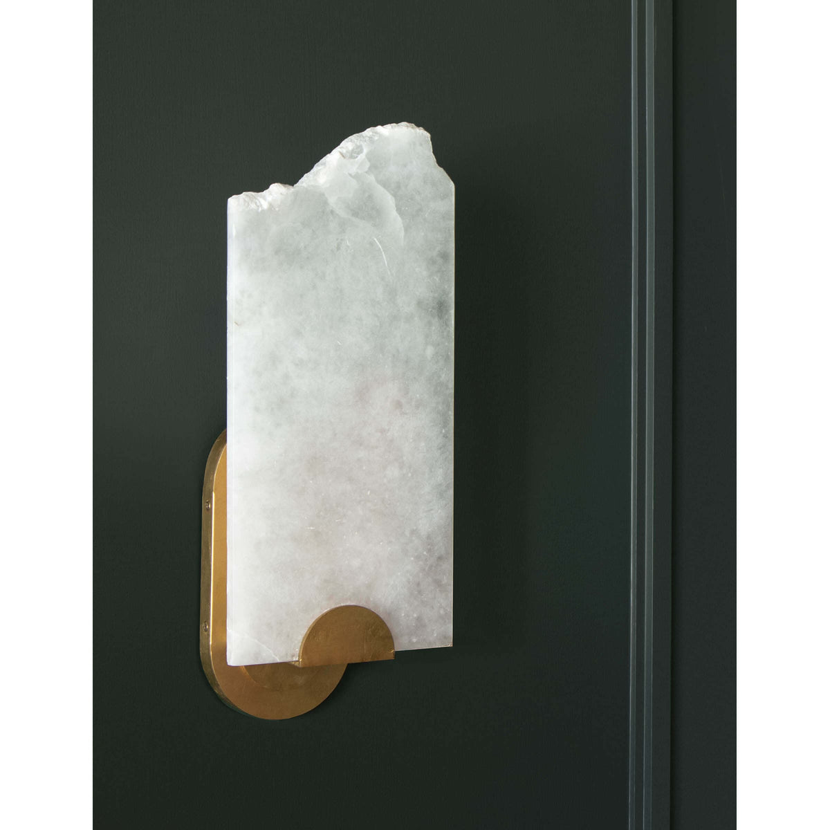 Jonah alabaster sconce with a raw broken edge, white veining, and a brass base on a dark wall.