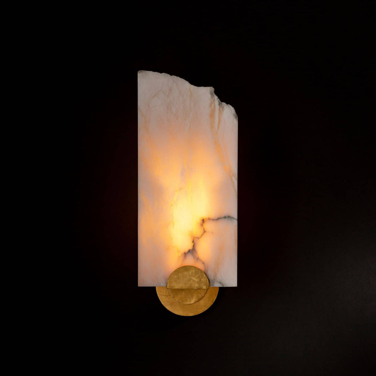 Jonah alabaster sconce with a warm glow, raw broken edge, and brass base.