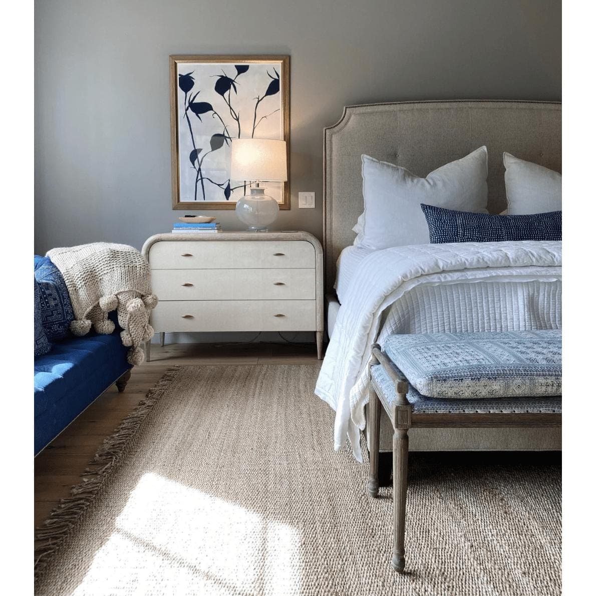 Beige hand-woven jute rug with fringe in a bedroom with a bed, bench, and dresser.
