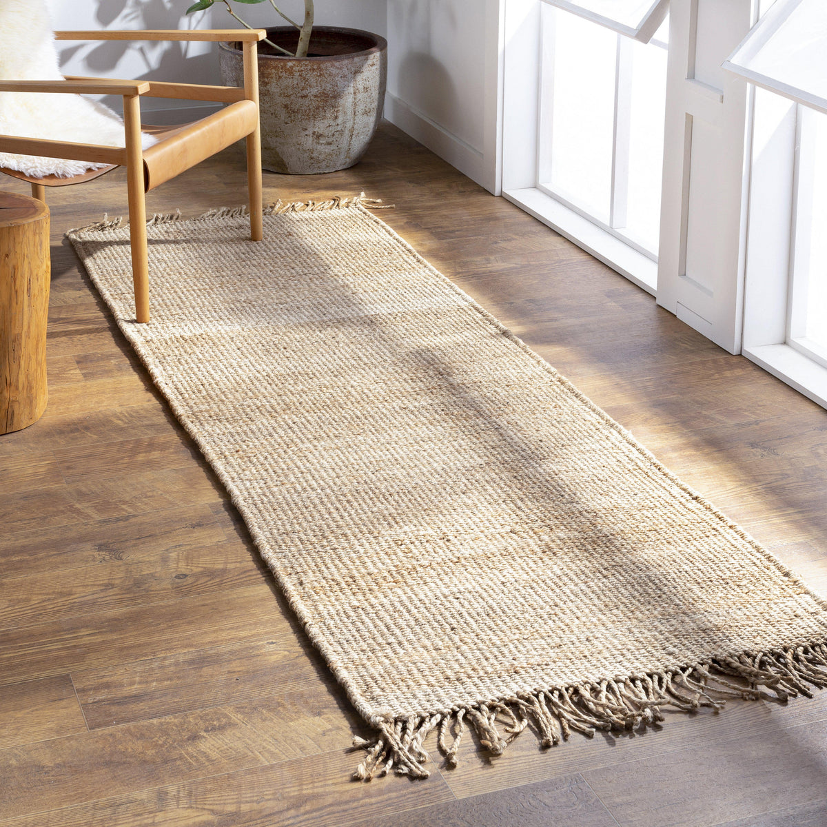 Beige, hand-woven jute runner rug with fringed ends on a wooden floor, adding natural charm.