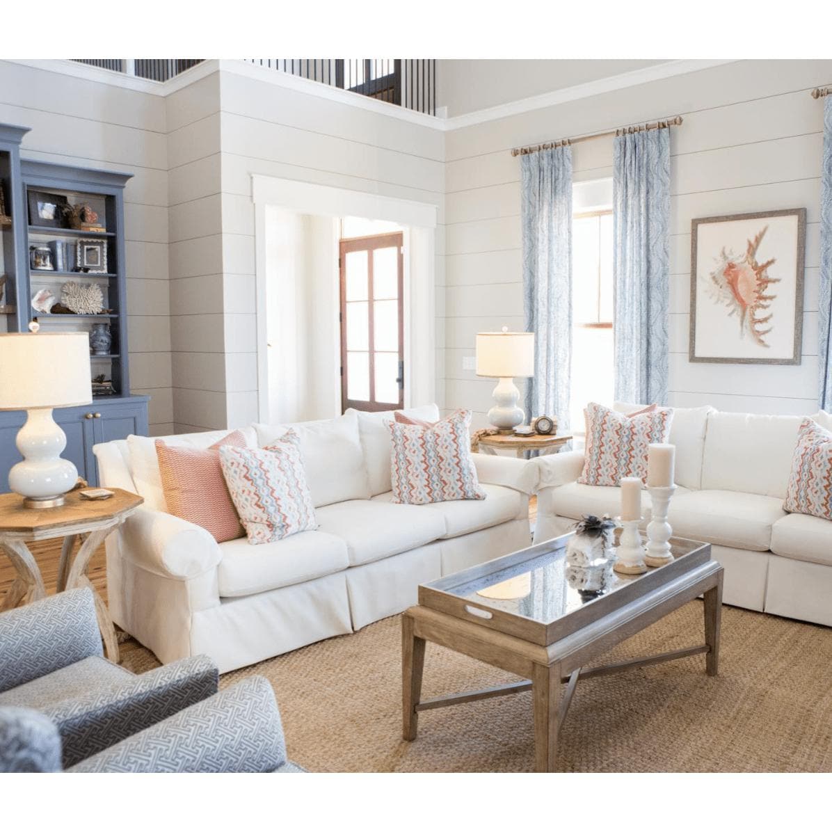 Tan hand-woven jute rug grounding a coastal-inspired living room with white sofas and blue accents.