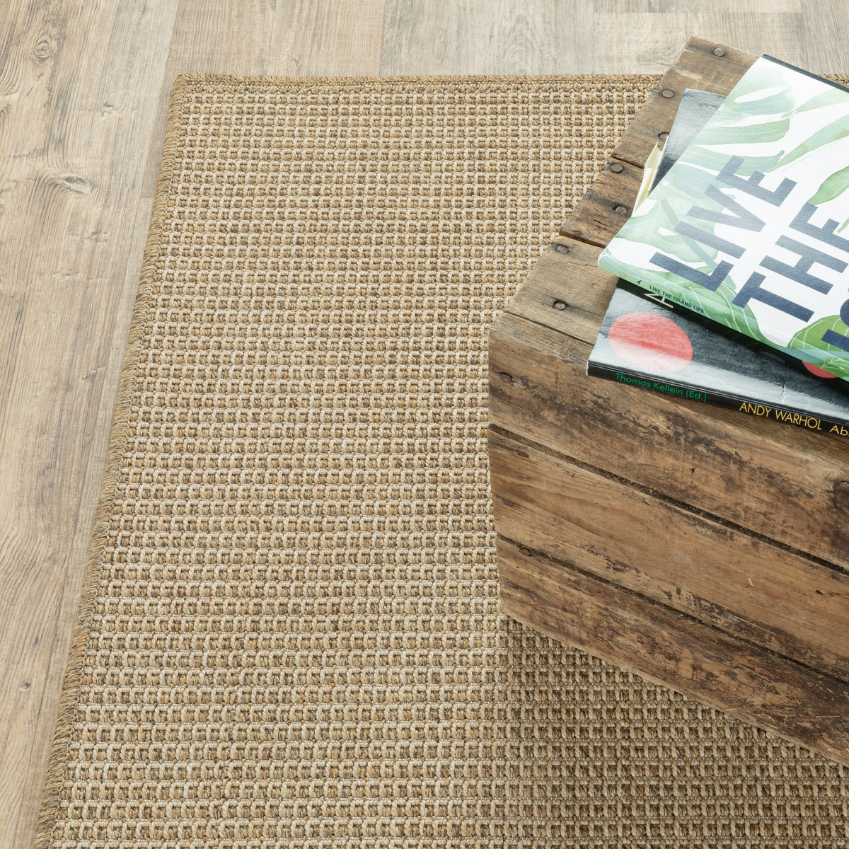 Karavia Sand outdoor rug, a woven polypropylene rug with a natural seagrass look, next to a rustic wooden crate.