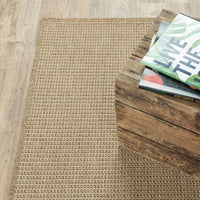 Karavia Sand outdoor rug, a woven polypropylene rug with a natural seagrass look, next to a rustic wooden crate.