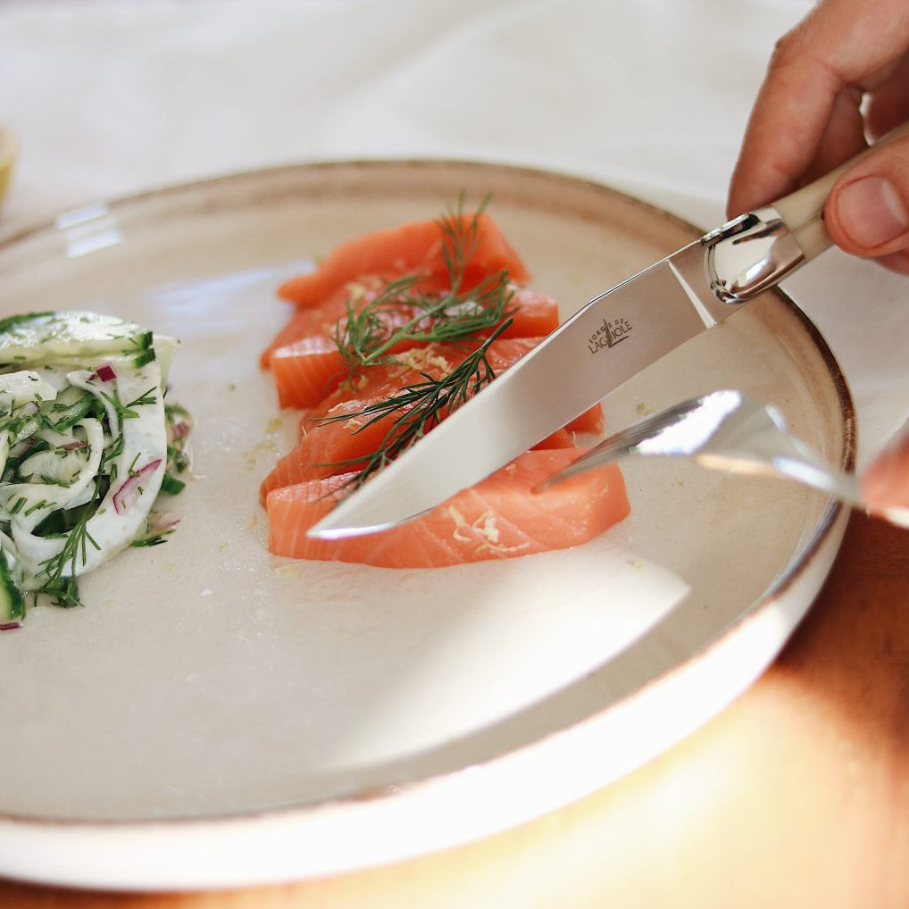 Person cutting a slice of salmon on a plate with a knife