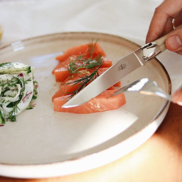 Person cutting a slice of salmon on a plate with a knife
