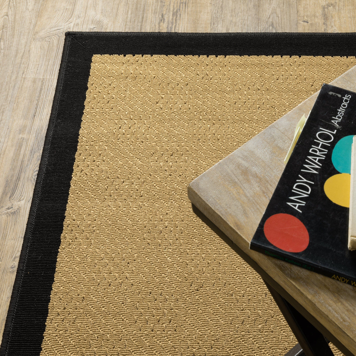 Lanai beige and black outdoor rug with a natural sisal-inspired weave, on a wood floor next to a table.