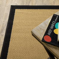 Lanai beige and black outdoor rug with a natural sisal-inspired weave, on a wood floor next to a table.