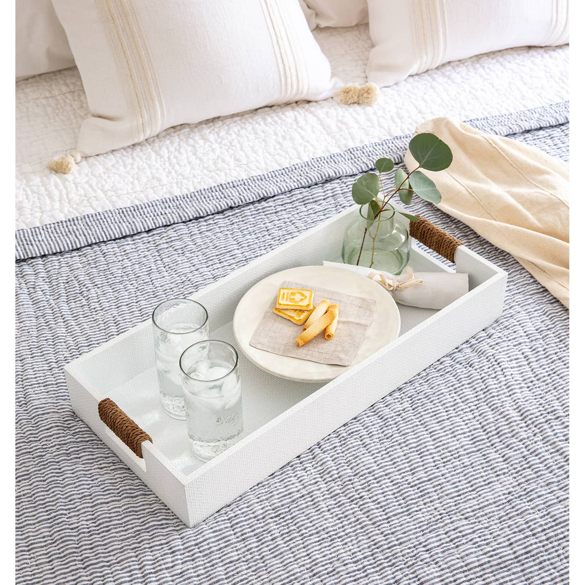 White Logia rectangle tray with rope-wrapped handles, holding glasses and snacks on a bed.