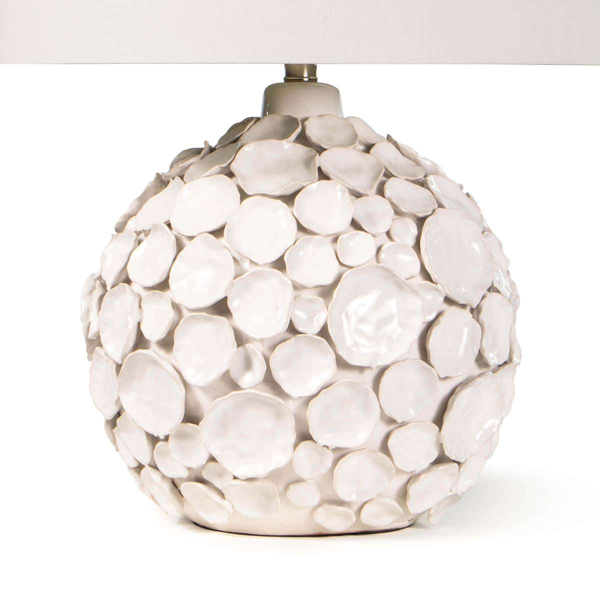 White ceramic table lamp with a round base covered in pinched disks and a linen shade.