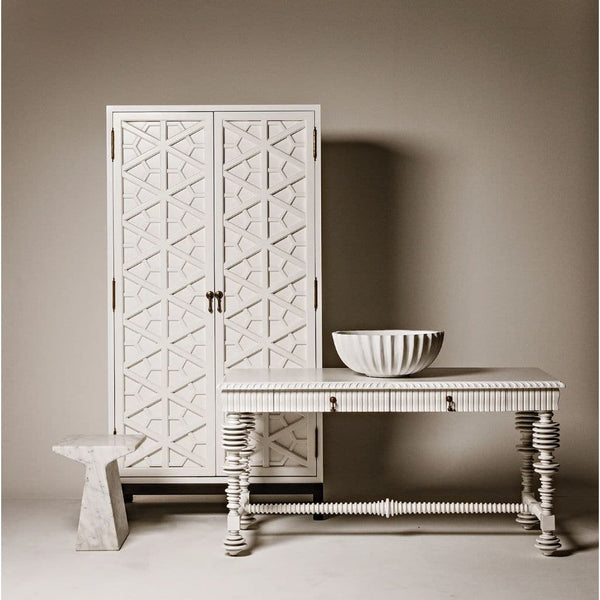 White mahogany hutch with hand-carved geometric doors, next to a matching console table and marble stool.