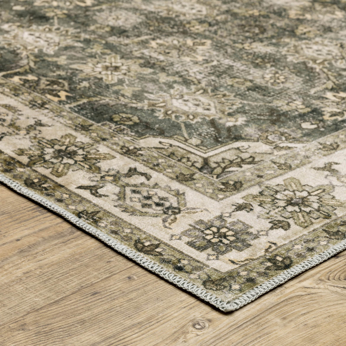 Distressed green and beige washable polyester rug with intricate floral patterns on a wooden floor.