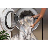 Hands placing a grey and multi-colored abstract polyester rug into a washing machine.