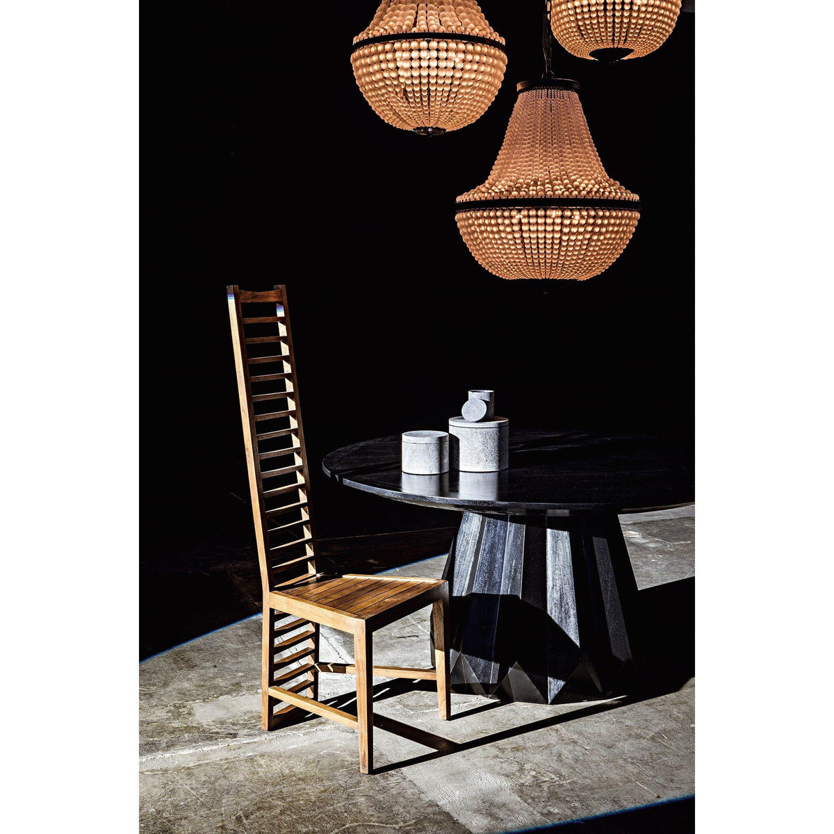 Three large, beaded Mist chandeliers with warm glow over a black steel table and tall wooden chair.