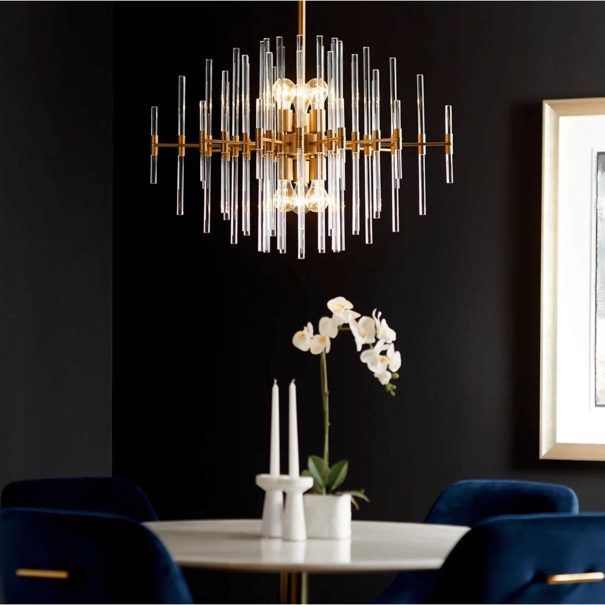Large aged brass chandelier with linear glass rods over a white marble table and blue velvet chairs.