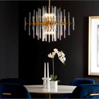 Large aged brass chandelier with linear glass rods over a white marble table and blue velvet chairs.