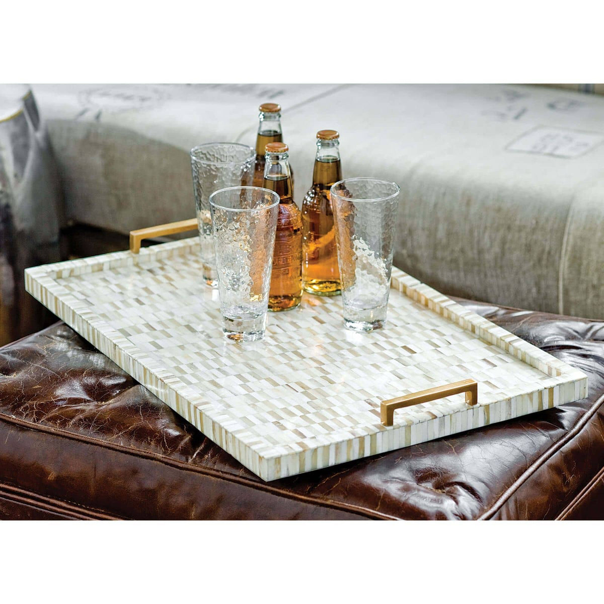 Multi-tone bone and brass tray with mosaic pattern, natural brass handles, on a leather ottoman.