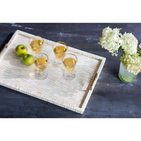Rectangular multi-tone bone and brass tray with mosaic pattern, brass handles, holding drinks, apples, and flowers.