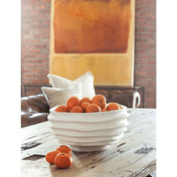White sculpted metal Nabu bowl with irregular grooves, holding oranges on a rustic wood table.