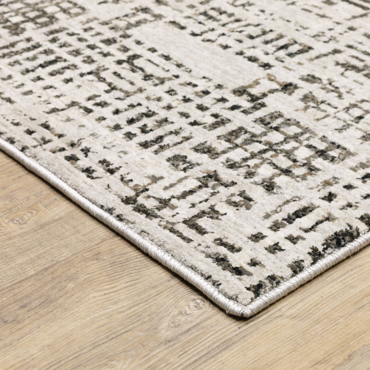 Ivory and charcoal abstract casual rug with a low-profile, textured polyester design on a wood floor.