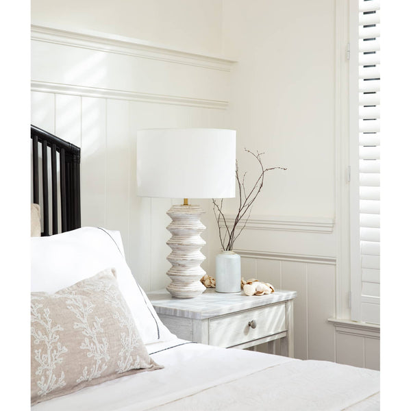 Nova Wood Table Lamp with white-washed carved wood body and natural linen drum shade on a bedside table.