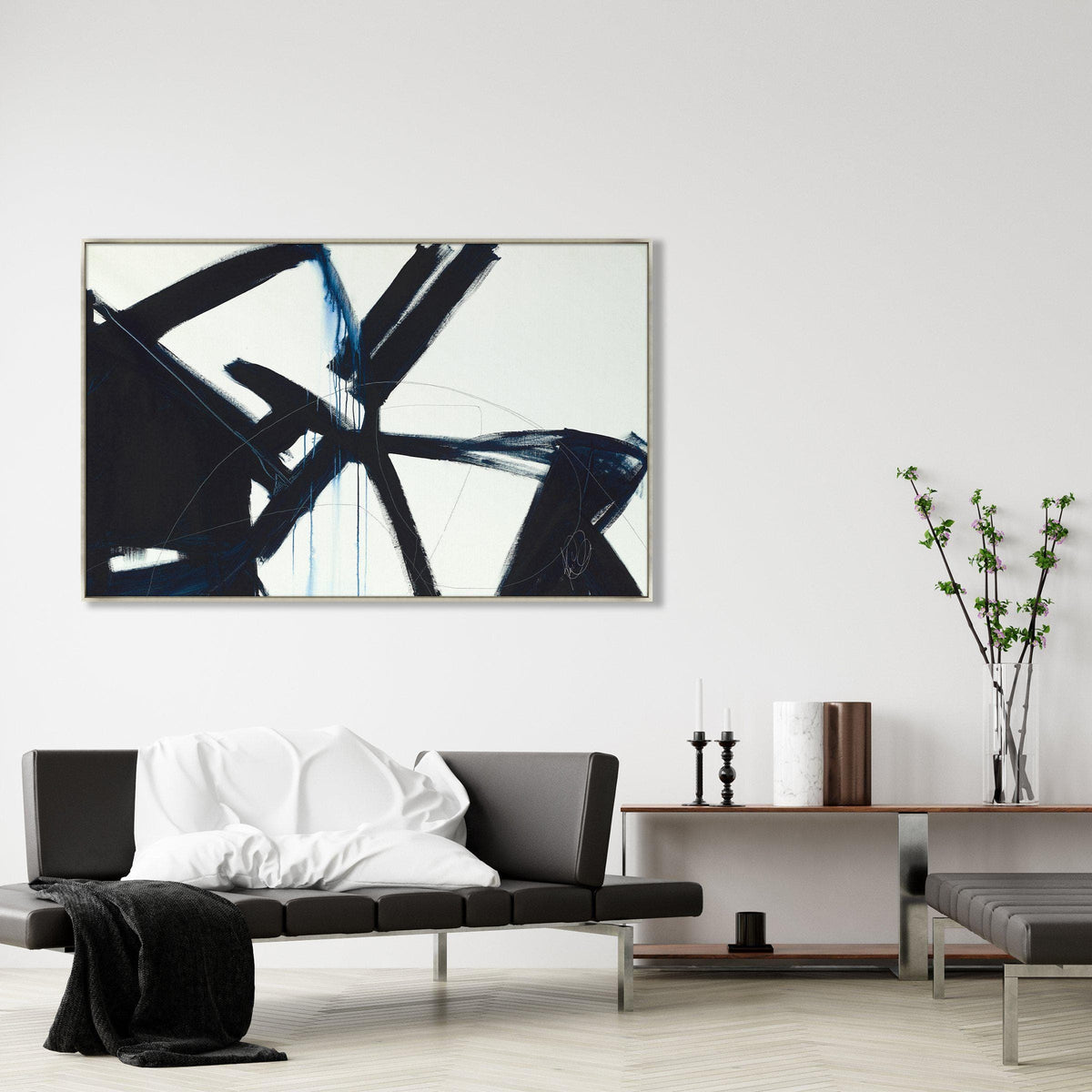 Abstract giclee canvas painting with bold black and blue brushstrokes in a gold frame, above a modern black leather sofa.