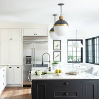 Otis Large Blackened Natural Brass pendant lights with white milk glass shades over a kitchen island.