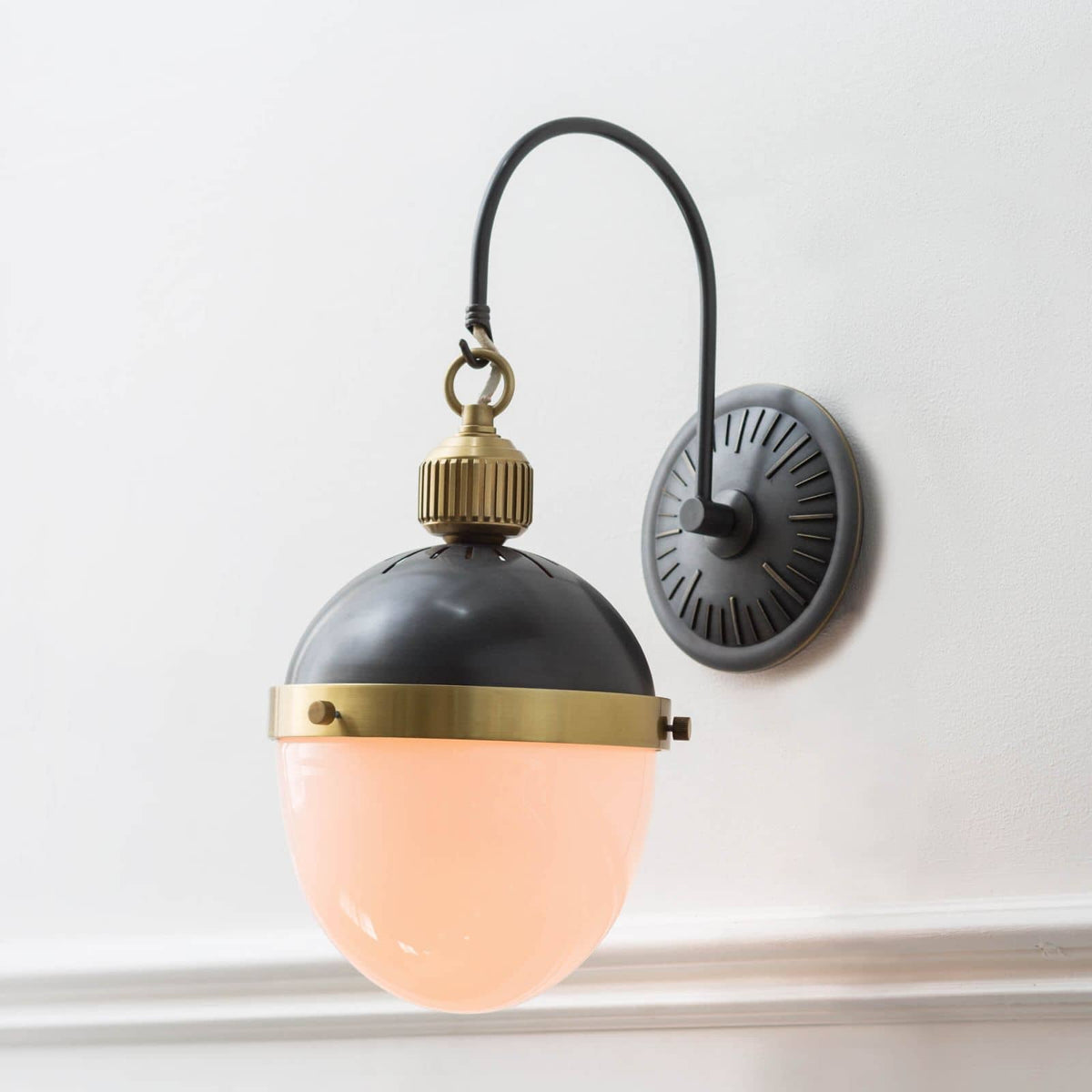 Otis Sconce with blackened brass and natural brass accents, featuring a curved arm and glowing opal glass shade.