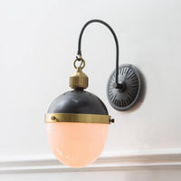 Otis Sconce with blackened brass and natural brass accents, featuring a curved arm and glowing opal glass shade.