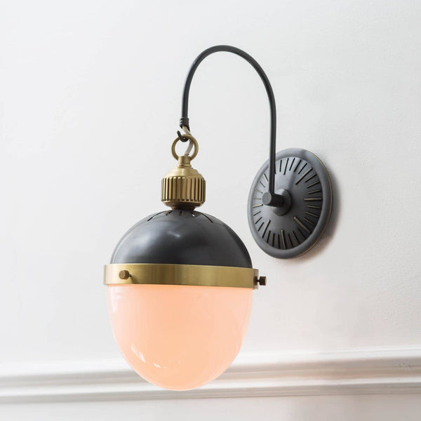 Otis Sconce with blackened brass and natural brass accents, featuring a curved arm and glowing opal glass shade.