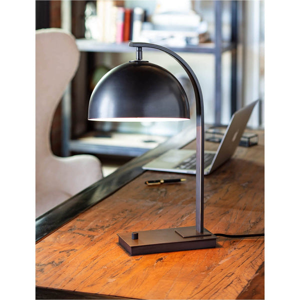 Otto Desk Lamp in oil rubbed bronze with a metal dome shade and curved neck on a wooden desk.