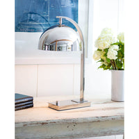 Otto desk lamp in polished nickel with a dome shade and curved neck on a distressed white table.