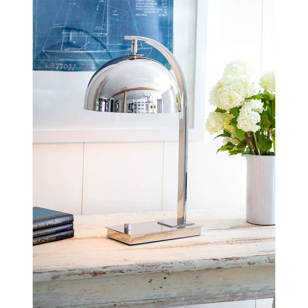 Otto desk lamp in polished nickel with a dome shade and curved neck on a distressed white table.