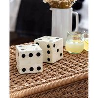 Pair of oversized bone dice with inlaid black dots on a woven surface.