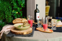 Table setting with a bowl of salad, glasses of pink and red drinks, and a bottle of wine outdoors.