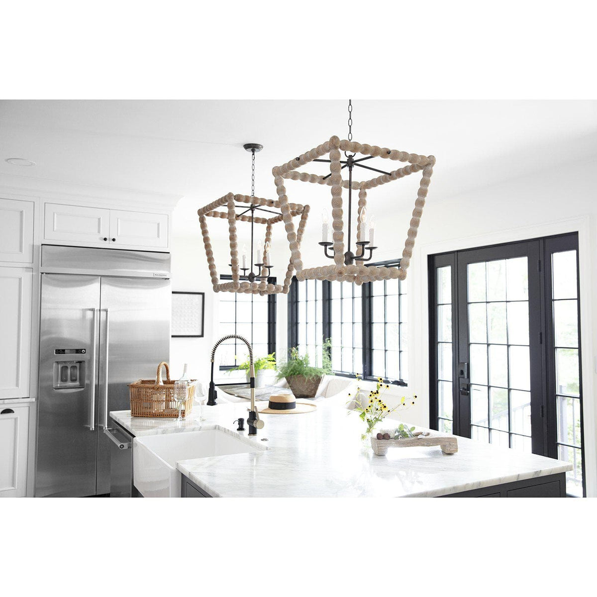 Two Perennial Lantern Natural chandeliers with wood beads and faux drip wax candle sleeves hang in a modern kitchen.