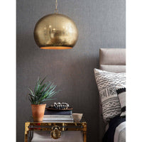 Natural brass pierced metal sphere pendant light with organic perforated design over a bedside table.