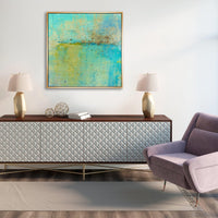 Abstract giclee canvas painting by Maeve Harris in turquoise and gold, framed above a textured white console.