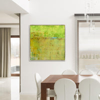 Abstract giclee canvas painting with vibrant green and yellow hues, framed above a wooden dining table.