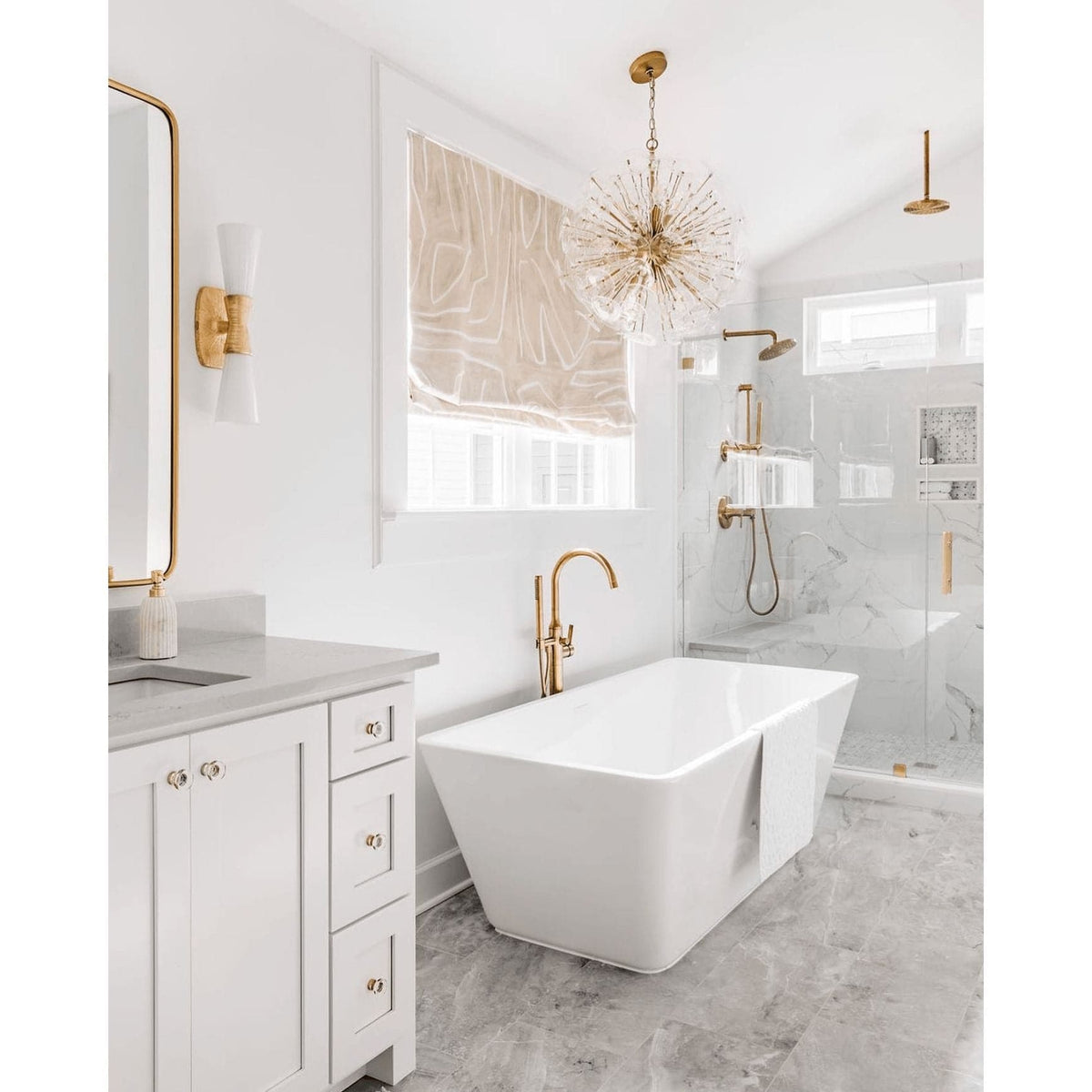 Poppy sputnik-style orb chandelier with clear glass discs and natural brass rods in a modern white bathroom.