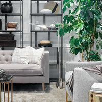 Raven Floor Lamp in polished nickel, 69.5" tall, with an adjustable, aerodynamic shade, next to a gray sofa.