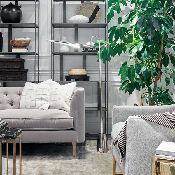 Raven Floor Lamp in polished nickel, 69.5" tall, with an adjustable, aerodynamic shade, next to a gray sofa.