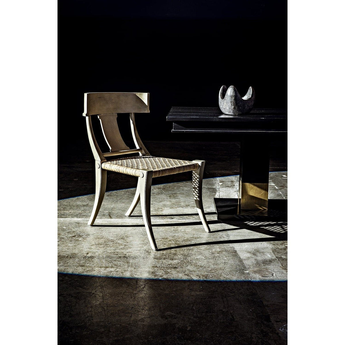 Ravenko black mahogany dining table with brass leg bands, next to a light-colored chair.