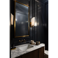 Rectangle natural brass mirror with a subtle frame, mounted above a marble vanity with a sink and brass fixtures.